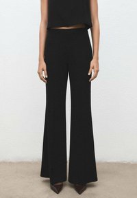 Pantalones acampanados negros de talle alto hechos de un material liso, con un corte de longitud completa y una silueta fluida.