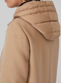 Manteau en laine beige avec une capuche matelassée de couleur marron clair. La capuche possède des coutures horizontales et une texture lisse, augmentant ainsi la chaleur.