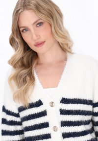Gestreifter cardigan in Weiß und Marineblau mit einer weichen, flauschigen Textur, V-Ausschnitt, langen Ärmeln und zwei dekorativen Knöpfen vorne.