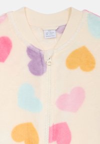 Fleece kindermantel met een crèmekleurige achtergrond en meerkleurige hartpatronen in roze, paars, blauw en geel; voorzien van een ritssluiting aan de voorkant.