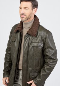 Braune Kunstpelzkragen grüne Lederjacke mit Reißverschluss und Knopfverschluss, mehreren Taschen und strukturiertem Finish. Schlichte Schnittführung.