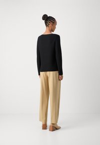 Schwarzer Langarmpullover mit quadratischem Ausschnitt, kombiniert mit beigen weiten Hosen und braunen Blockabsatzschuhen, von hinten betrachtet.