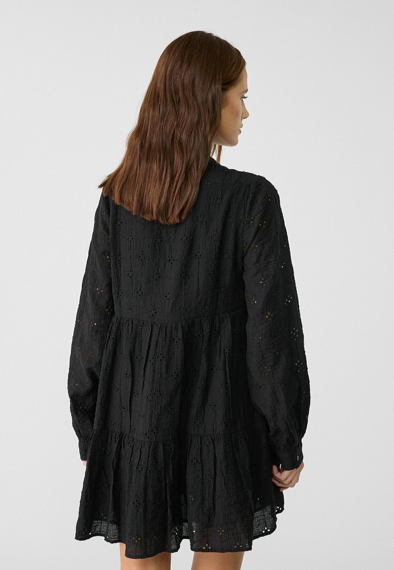 Abito nero con un motivo testurizzato a broderie anglaise. Presenta maniche lunghe, una gonna a strati e una vita arricciata.