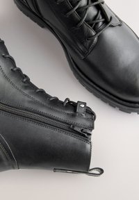 Zwarte leren enkellaarzen met veters aan de voorkant, zijrits en een geribbelde rubberen zool. Voorzien van een lusje voor gemakkelijk aan- en uittrekken.