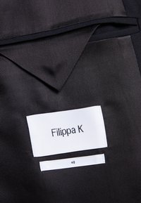 Schwarzer, strukturierter Stoff mit einem weißen Etikett, auf dem "Filippa K" steht, sowie einem Größenetikett "48" darunter. Minimalistisches Design, maßgeschneiderter Look.