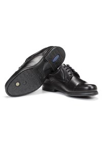 Zapatos de vestir de cuero negro con punta redonda, cordones y suelas de goma texturizadas que presentan dos acentos circulares. Acabado liso con detalles de costura.