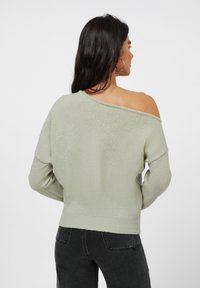 Lys grønn strikkegenser med off-shoulder design, lange ermer og ribbestrikket kant. Myk tekstur, avslappet passform og minimalt med detaljer.