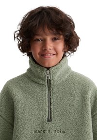 Zielony sweter polarowy z wysokim kołnierzem i półzamek, o fakturowanej powierzchni oraz nadrukowanym ciemnoszarym logo na wysokości klatki piersiowej.