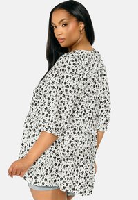 Vit blus med svart blommönster, löst sittande, korta puffärmar, samlad detalj på ryggen, lättviktig tyg och rundad nederkant.