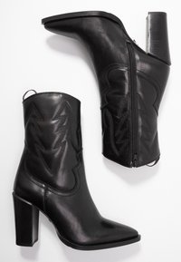 Une paire de bottes noires en cuir mi-mollet avec des talons carrés, des bouts pointus, une fermeture éclair sur le côté et des motifs zigzag cousus sur la tige.