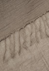 Tissu brun texturé avec bords effilochés. Matière douce et légère présentant un motif froissé. Les bords comportent des fils lâches pour plus de détail.