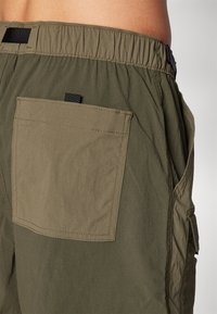 Ελαιώδους πράσινου σορτς με ελαστική μέση, που διαθέτει μια μεγάλη πίσω τσέπη και πλευρικές ραφές. Κατασκευασμένο από ελαφρύ, υφασμάτινο υλικό.