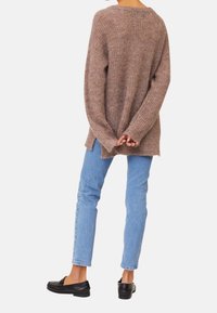 Brun stickad tröja med en lös passform, långa ärmar, sidofickor och en strukturerad yta. Tillsammans med ljusblå jeans och svarta loafers.