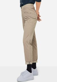 Pantaloni beige in cotone, con vita alta, risvolti e due tasche posteriori. Abbinati a sneaker bianche.