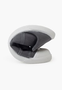 Zapato de tela gris con un diseño flexible, suela de goma blanca, superficie texturizada y puntera redondeada, mostrando una posición plegada.