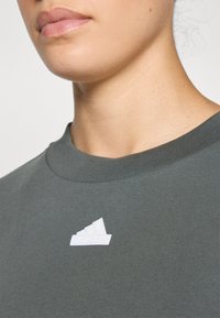 Σκούρο πράσινο μπλουζάκι με στρογγυλή λαιμόκοψη. Διαθέτει λευκό λογότυπο Adidas στη αριστερή πλευρά. Ιδαίτερα ομαλή υφή, χαλαρός σχεδιασμός.