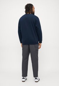 Marineblaues Sweatshirt mit gerippten Bündchen und Saum, kombiniert mit dunkelgrauen Cargo-Shorts, die über mehrere Taschen verfügen. Bequeme Schuhe runden das Outfit ab.