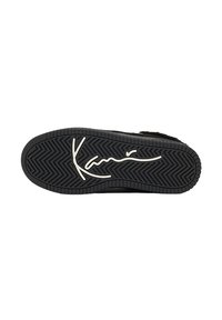 Svart gummisåle til sneakers med et fiskebeinmønster og en fremtredende signaturdesign i hvitt over midten.