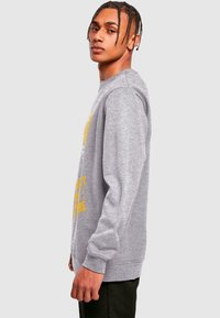 Šedá mikina s dlouhými rukávy, zdobená žlutým grafickým potiskem. Design s crew neck a volným střihem, vyrobena z měkké, texturované látky.