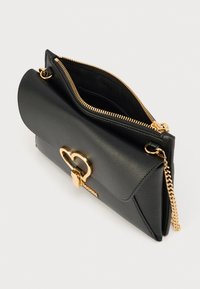 Μαύρη δερμάτινη τσάντα χειρός με χρυσό κούμπωμα σε σχήμα καρδιάς, άνοιγμα με φερμουάρ και αλυσίδα λουρί. Στερεή σχεδίαση με απαλό υφή.