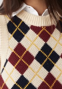 Pull en laine à motif losanges argyle avec une base crème ornée de losanges bleu marine foncé, bordeaux et jaune. Col côtelé et tricot texturé.