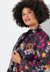 Chaqueta negra con llamativos patrones gráficos en rosa, blanco y naranja, con solapa en pico y textura suave y brillante.