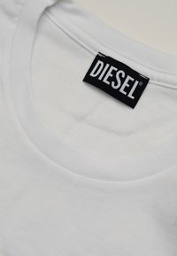 Primo piano di una camicia bianca a girocollo con un'etichetta nera rettangolare del marchio "DIESEL" cucita all'interno del colletto.
