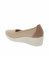 Zapatilla beige tipo slip-on con parte superior de malla texturizada y acento de ante en el talón. Presenta una suela en cuña blanca con patrones de agarre visibles.