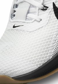 Sapatilha desportiva branca com upper em malha, detalhes pretos, superfícies texturizadas e sola em borracha. Apresenta o logótipo da Nike de lado.
