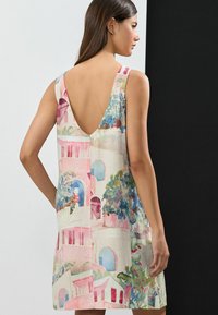 Ein ärmelloses Leinenkleid mit einem lebhaften Aquarellmuster von Gebäuden und Grünanlagen, einem tiefen V-Ausschnitt auf der Rückseite und geradem Saum.