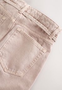 Pantalon en denim beige clair montrant la poche arrière, les passants de ceinture et les coutures de la ceinture sur un fond clair uni.