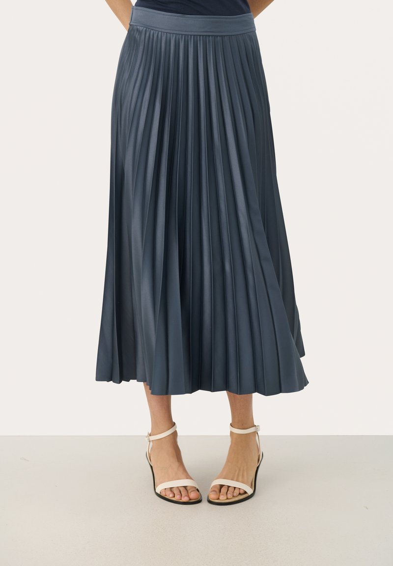 Jupe midi plissée en satin bleu foncé, dotée d'une taille large et d'un design fluide. Portez-la avec des talons blancs à lanières.