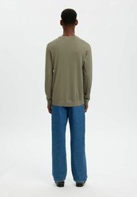 Pull à manches longues vert olive avec col rond, poignets côtelés et coupe décontractée, associé à un jean en denim bleu à jambes larges.