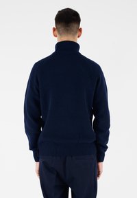 Maglione a collo alto in maglia blu navy, con polsini e fondo a coste. Presenta un motivo strutturato e maniche raglan.