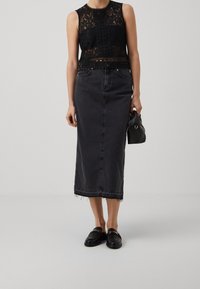 Haut sans manches en dentelle noire avec des motifs complexes, associé à une jupe midi en denim foncé avec un ourlet effiloché. Des mocassins noirs complètent la tenue.