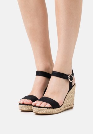 Sandalias cuña negras con parte superior de tela, correa al tobillo con hebilla redonda y suela de cuerda trenzada. Diseño de punta abierta con acolchado mínimo.