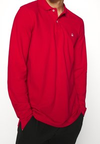 Czerwona, długosleeve polo z miękkiego materiału, z trzema guzikami przy dekolcie i małym haftowanym logo na piersi.