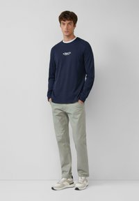 Marineblaue Langarm-T-Shirts mit einem weißen Rundhalsausschnitt und Logo, kombiniert mit hellgrünen Hosen und grauen Sneakers mit weißen Akzenten.
