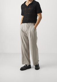 Polo negro de punto abierto de manga corta con cuello, combinado con pantalones beige claros con pliegues y mocasines negros con un acento decorativo de metal.