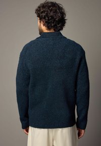 Pulover tricotat texturat, de culoare albastru închis, cu guler și mansete cu dublură. Are o croială lejeră și este realizat dintr-un amestec de lână pentru căldură.