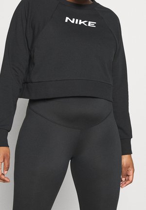 Zwart cropped Nike-sweatshirt en zwarte leggings met hoge taille gedragen door een staande persoon tegen een effen achtergrond.