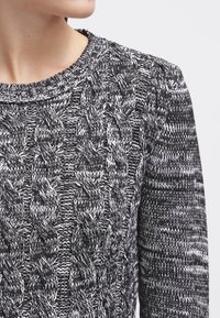 Maglione lavorato a maglia bianco e nero con un morbido motivo a treccia, scollatura rotonda e polsini a coste, caratterizzato da una finitura testurizzata.