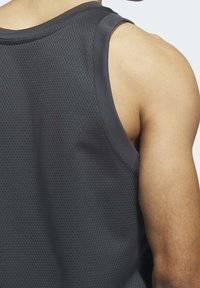 Tmavě šedý atletický top bez rukávů s texturovaným, prodyšným designem z síťoviny. Široké armhole a hladký výstřih dokončují střih.