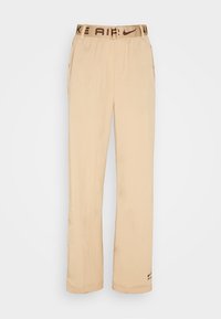 Béžové kalhoty Nike s širokým střihem, elastickým pasem se hnědým logem a bočními kapsami. Hladká textura a lehký materiál.