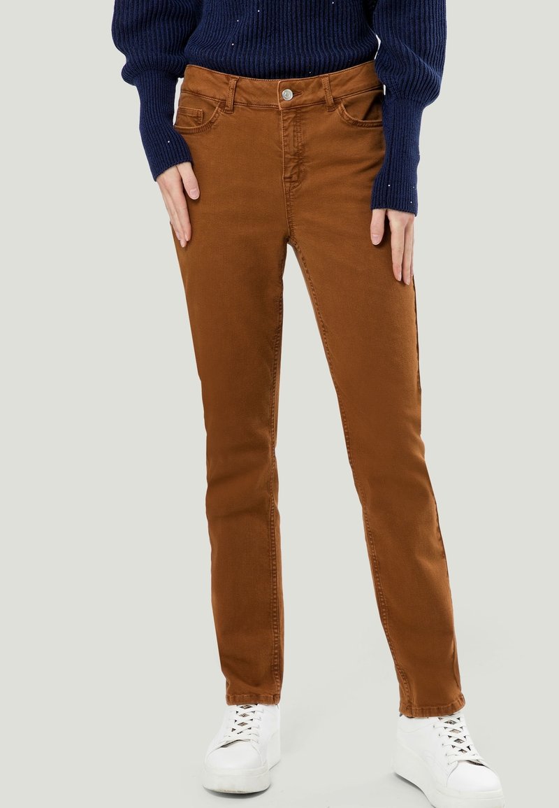Pantalones de algodón marrones, de corte ajustado, con una textura suave, que presentan bolsillos frontales y un cierre de botón, combinados con zapatillas blancas.