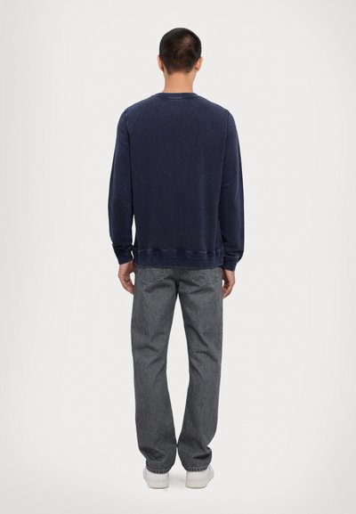 Marineblå sweatshirt med lange ærmer, rund halsudskæring og ribbede manchetter; iført med grå jeans og hvide sneakers. Glat tekstur.