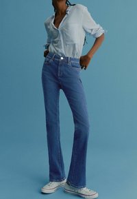 Chemise boutonnée à rayures bleu clair avec une coupe décontractée. Jean flare taille haute en denim bleu moyen. Baskets blanches avec des accents rouges.