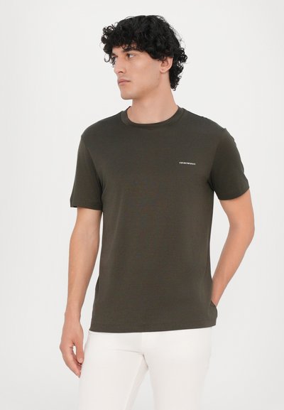 T-shirt en coton vert olive avec un col rond, des manches courtes et un petit logo sur la poitrine. Texture lisse et design ajusté.