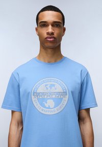 Světle modré bavlněné tričko s kulatým výstřihem a krátkými rukávy, s kulatým grafickým potiskem Antarktidy a logem v kontrastních barvách.