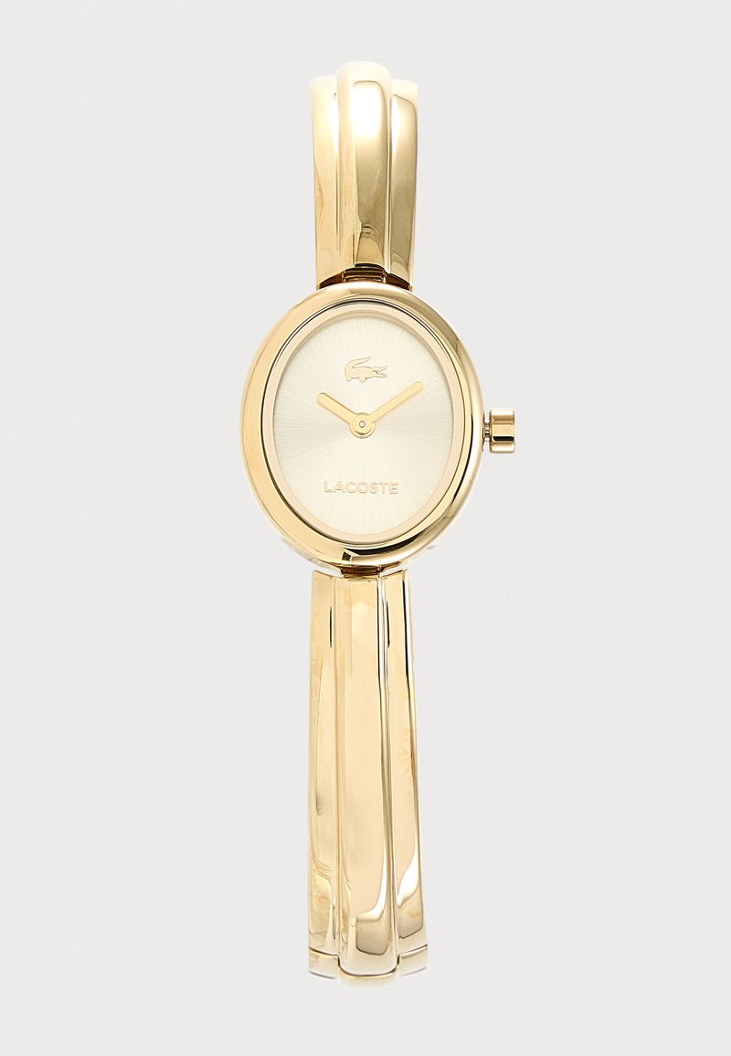 Montre Lacoste dorée avec cadran ovale, aiguilles dorées simples et bracelet métallique fin et brillant.